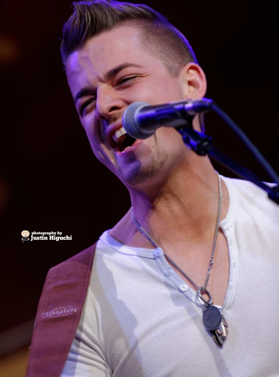 a man in a white t - shirt singing with his mouth open