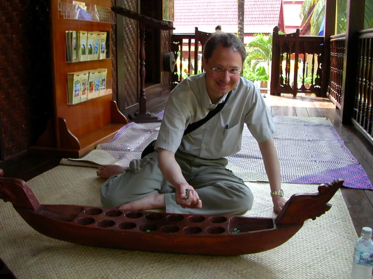 a man sitting on the ground in a room with a wooden boat in it