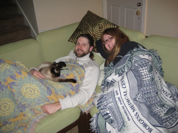 a man and woman lying on a couch holding a cat