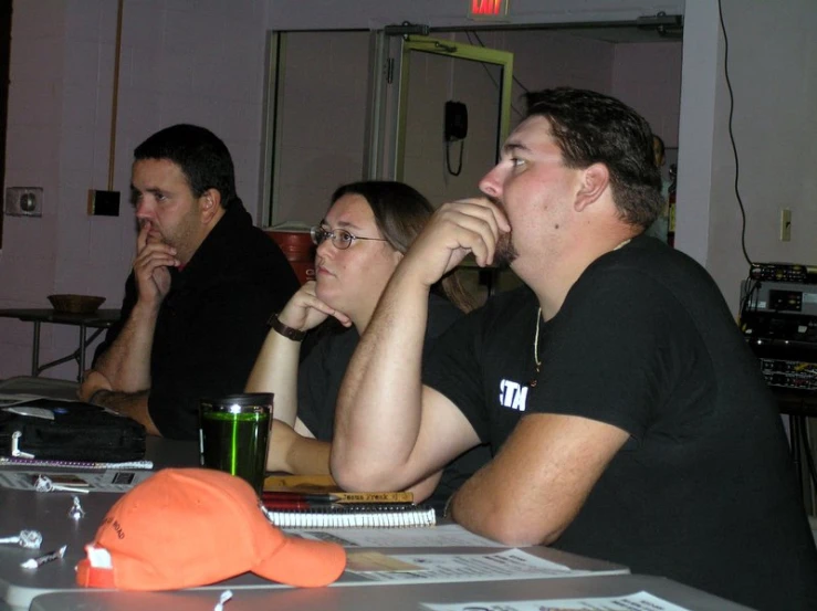 a group of people sitting at a table, with each holding their face to their ears