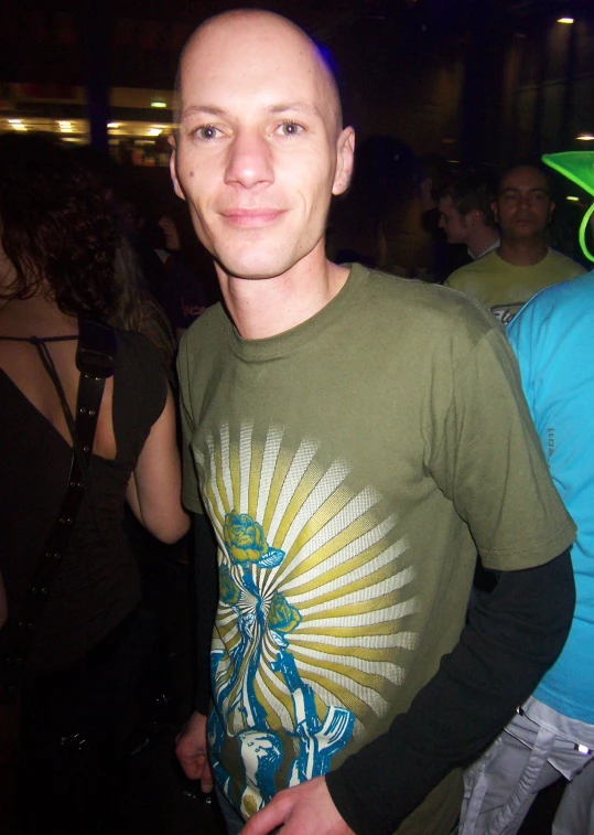 a bald man standing with one leg crossed wearing green t shirt