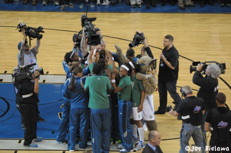 a crowd of people standing around a basketball court with camera on their laps