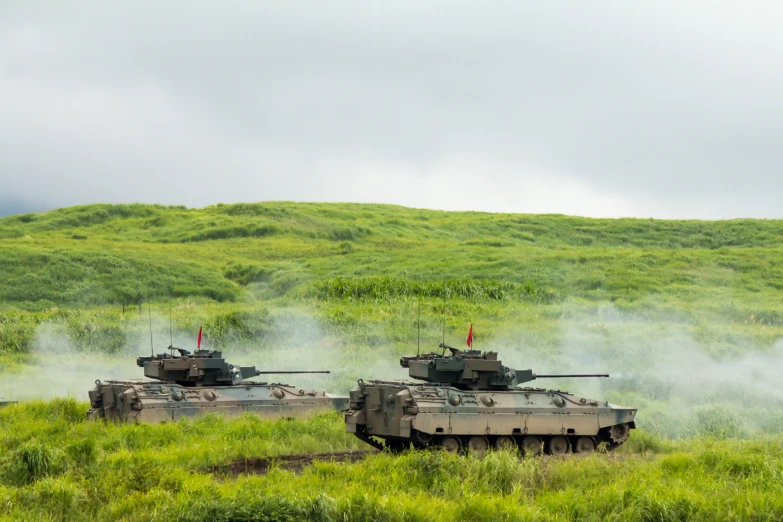 two army tanks passing through a grassy field
