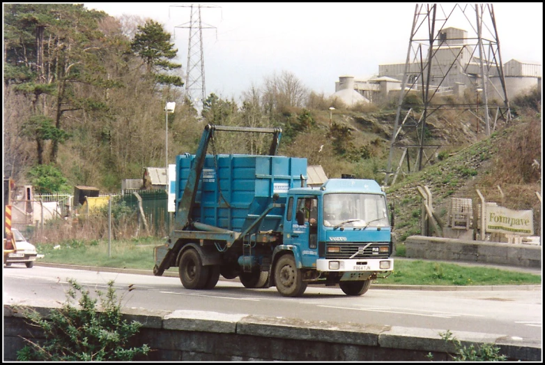 a blue truck traveling down a road past a wooded area