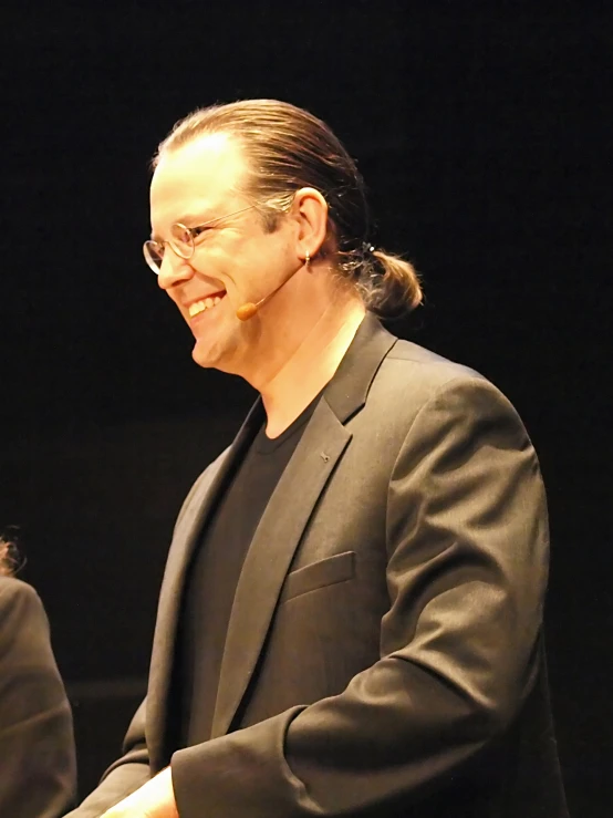 a man with a ponytail stands smiling at a stage