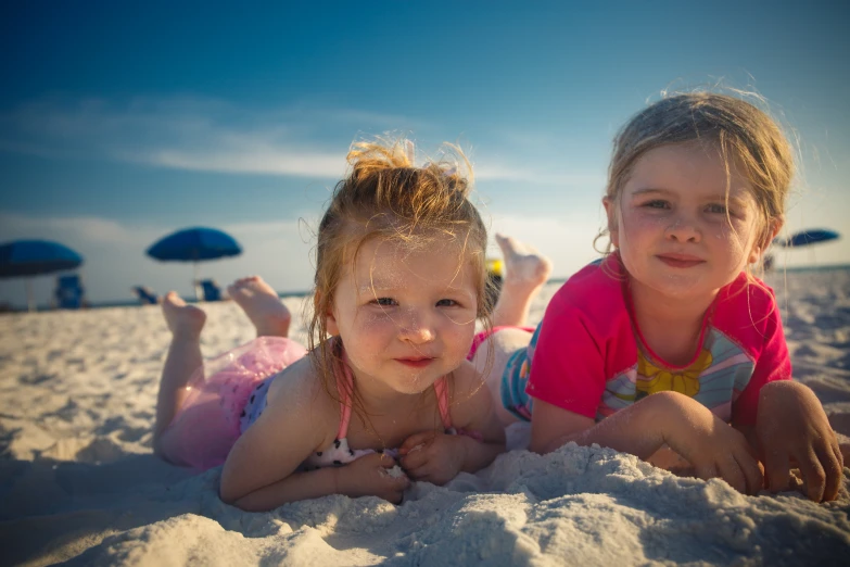 two girls laying on the beach with umbrellas