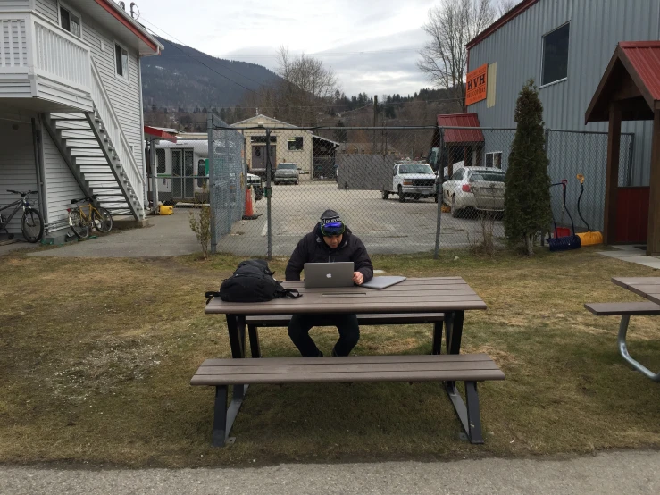 a man sitting at a picnic table outside while looking at his laptop