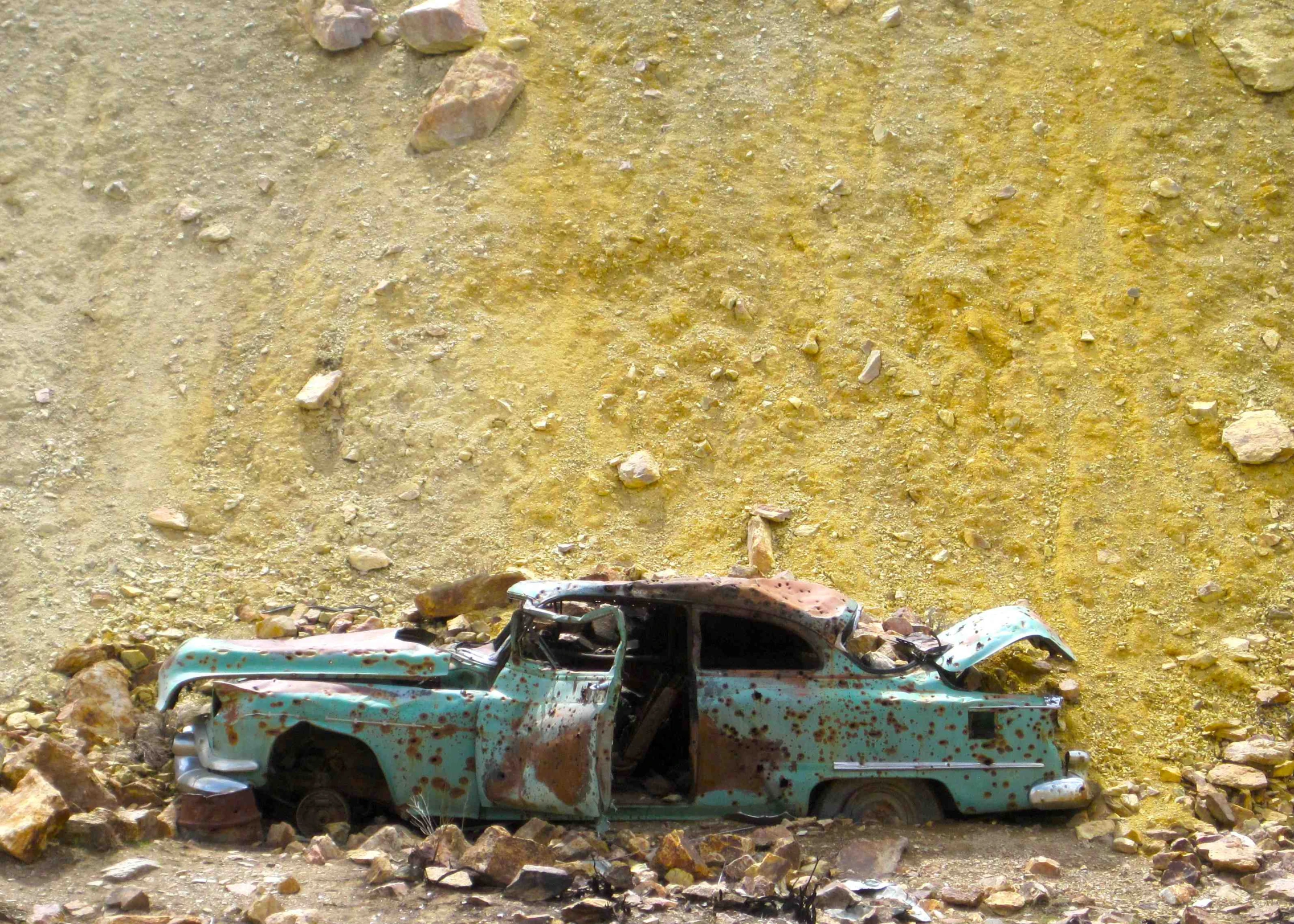 an old run down truck sitting in the dirt next to a yellow wall