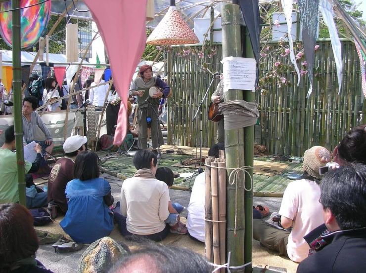 people sitting and standing around an area of bamboo poles