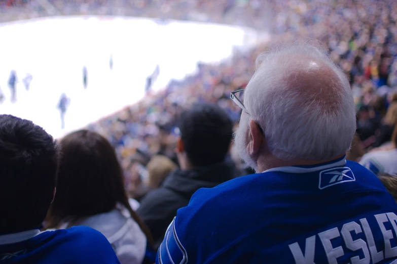 an old man wearing a blue jersey sitting next to a large group of people