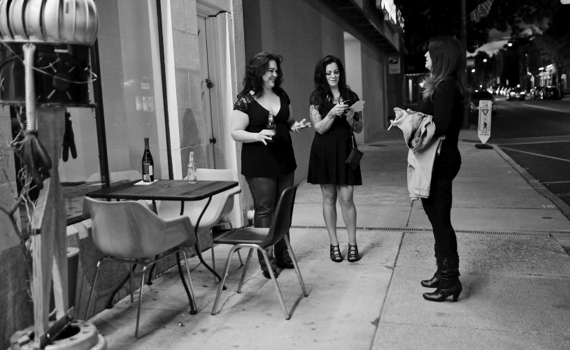 two women on cellphones and one man on the sidewalk