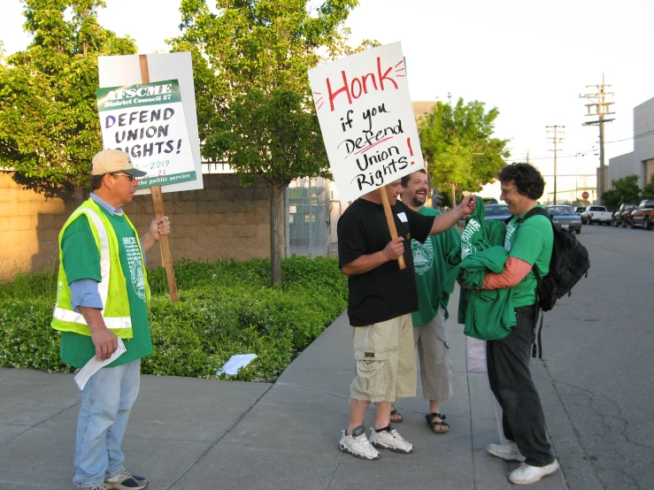 men with protest signs on their backs, one holding a sign that says honk