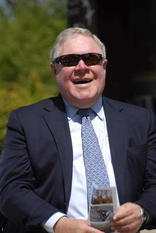 a man in sunglasses is wearing a suit and holding a white card