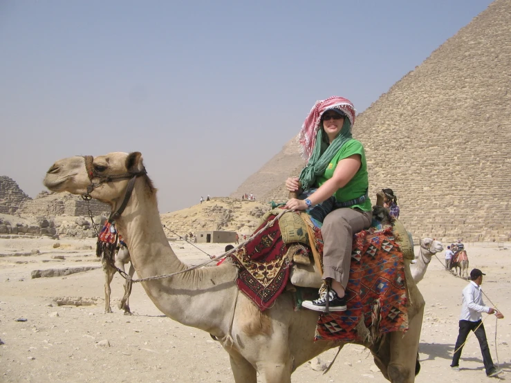 a woman sitting on top of a camel next to a pyramid