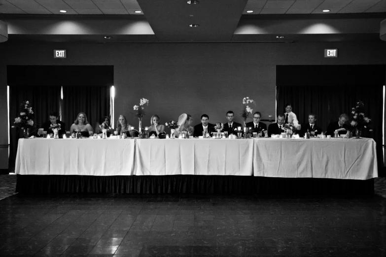 a number of people sit at a large table with two men standing behind it
