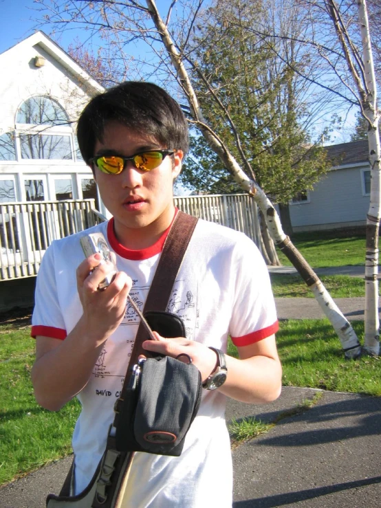 a man in a white t - shirt and sunglasses holds a cell phone