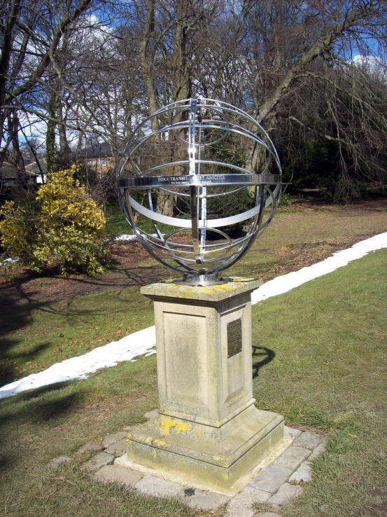 a sculpture of a sphere on a stone block in the grass