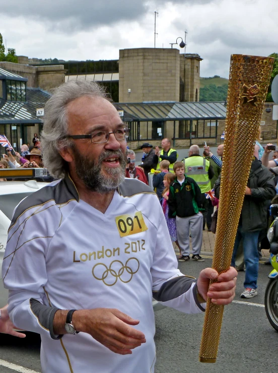 a man with white beard and glasses holds a olympic torch in his hand