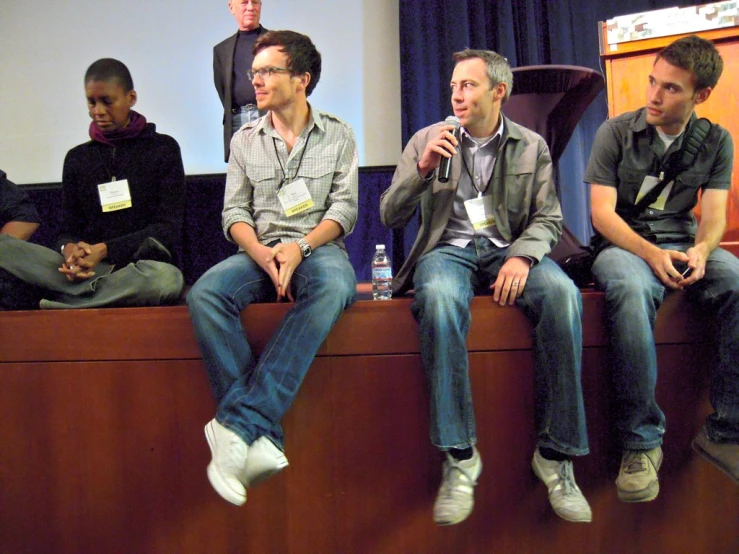 five men in an audience listening to a speaker