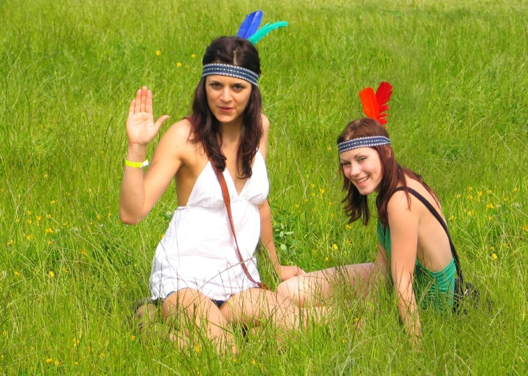 two young women with feather headbands sitting in a field