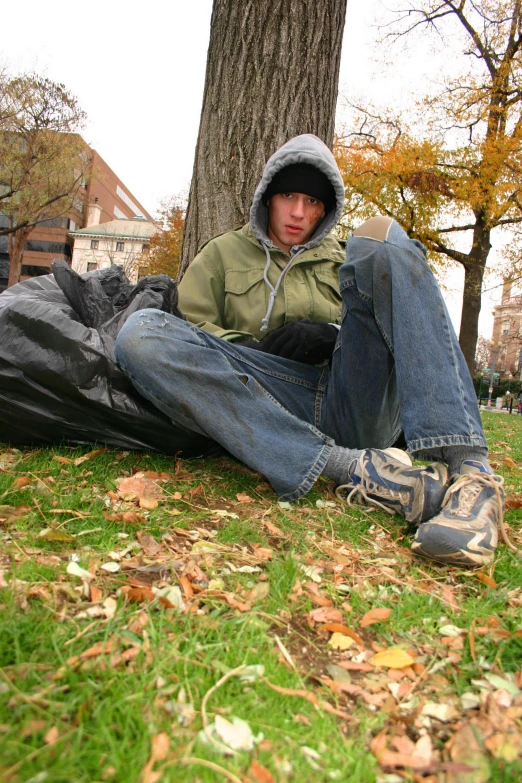 the young man is sitting in the park wearing a jacket