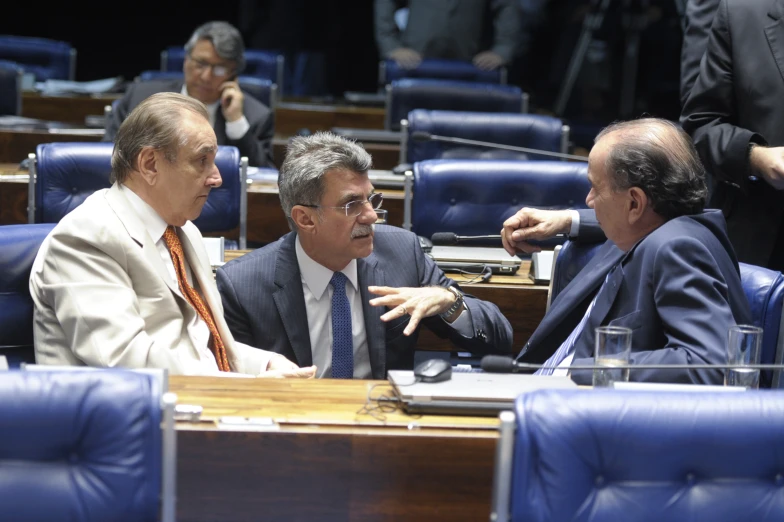 three men sit in an auditorium talking