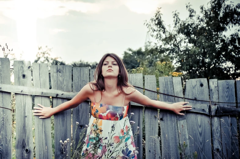 a woman leans on a wooden fence