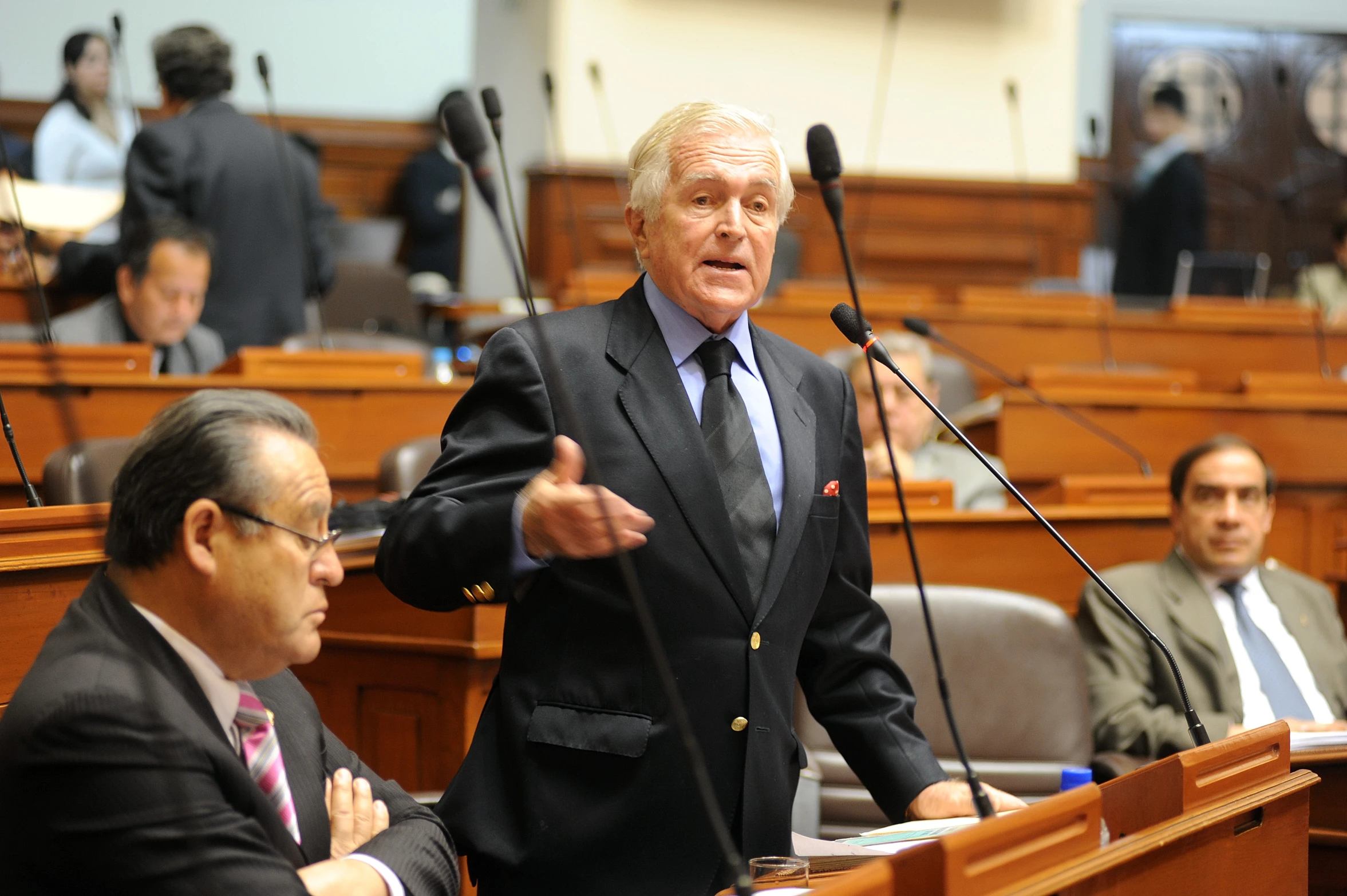 a man with grey hair and a black suit and tie speaking in the assembly chamber