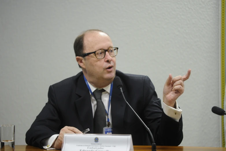 a man in a suit speaks while gesturing and pointing