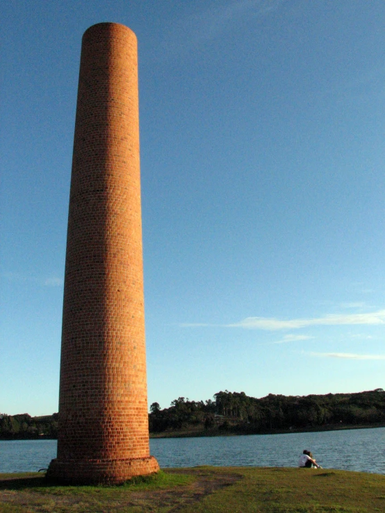 a tall brick tower standing in the middle of a field near a body of water