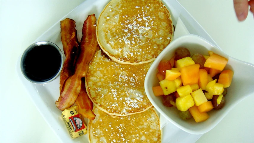 an oatmeal topped pancake next to fruit and bacon