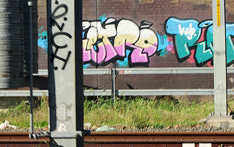 graffiti painted on a brown wall above train tracks