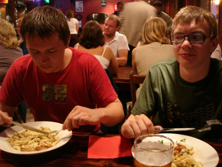 two boys sitting at a table eating macaroni and cheese