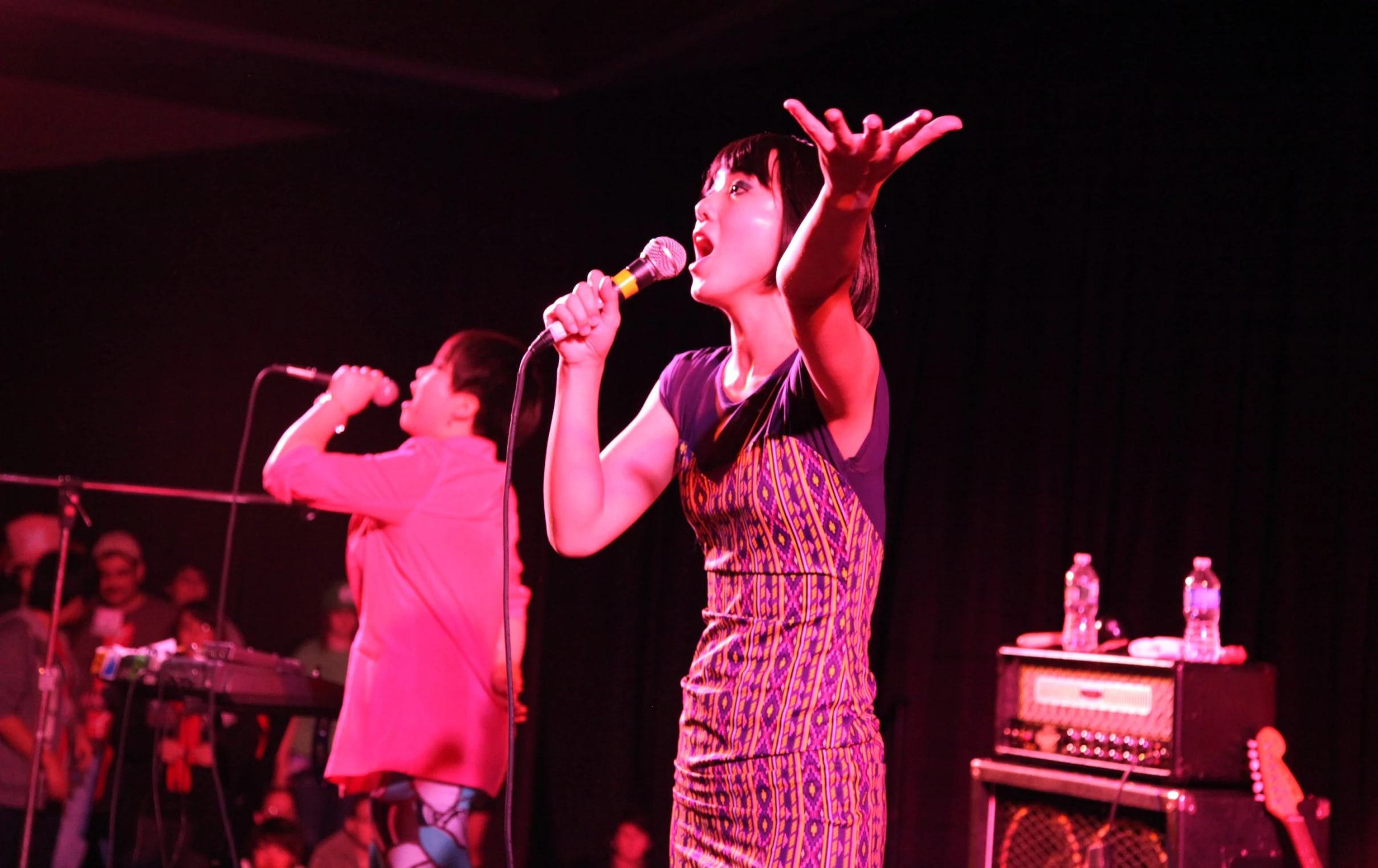 two people standing next to each other singing on a microphone