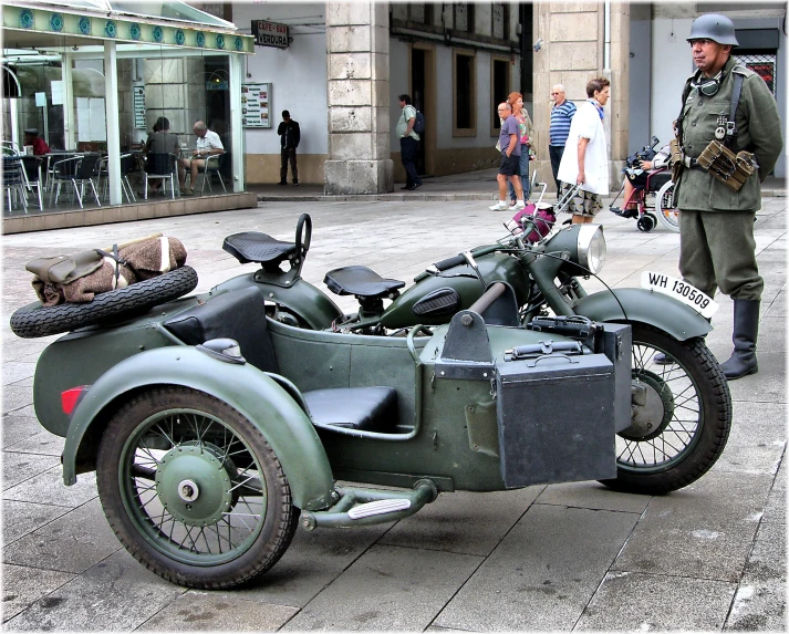 an army motorcycle is parked on the street while a soldier stands in the background
