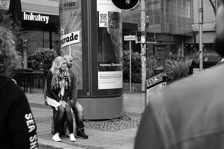 two people sitting on a bench on a street corner