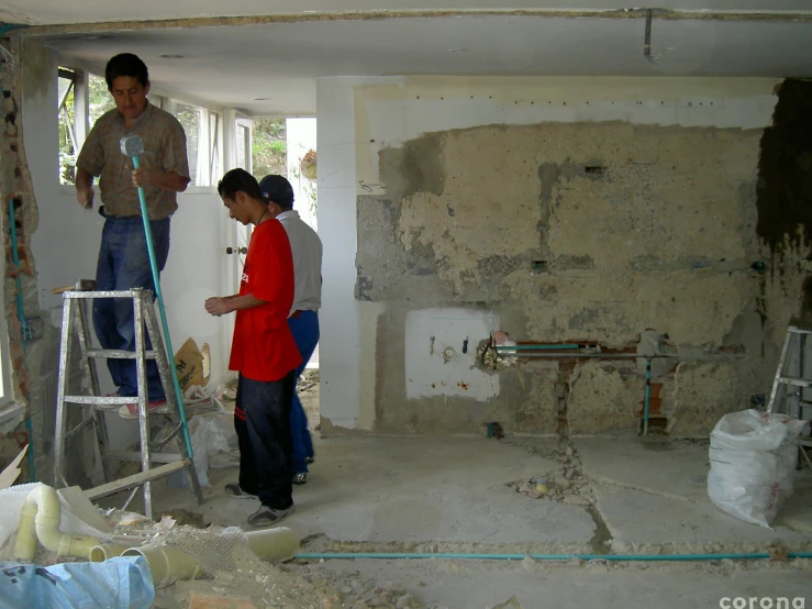 two men stand at the top of ladder in an unfinished room with plaster all over it