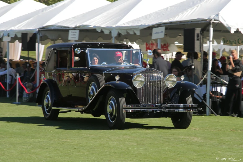 an old fashioned black and silver car traveling through a grassy area