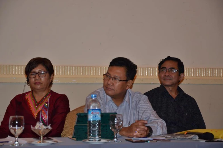 three people at a table talking while others look on