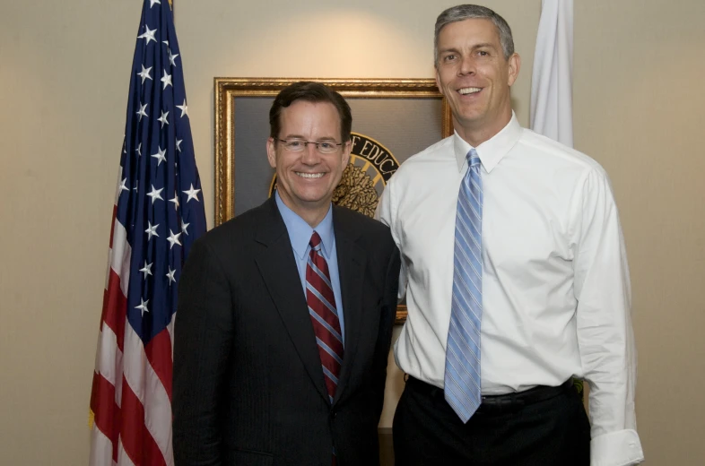 two men standing side by side in front of an american flag