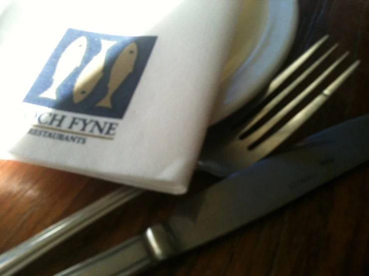 a napkin with a fish logo on it sits between two silver fork