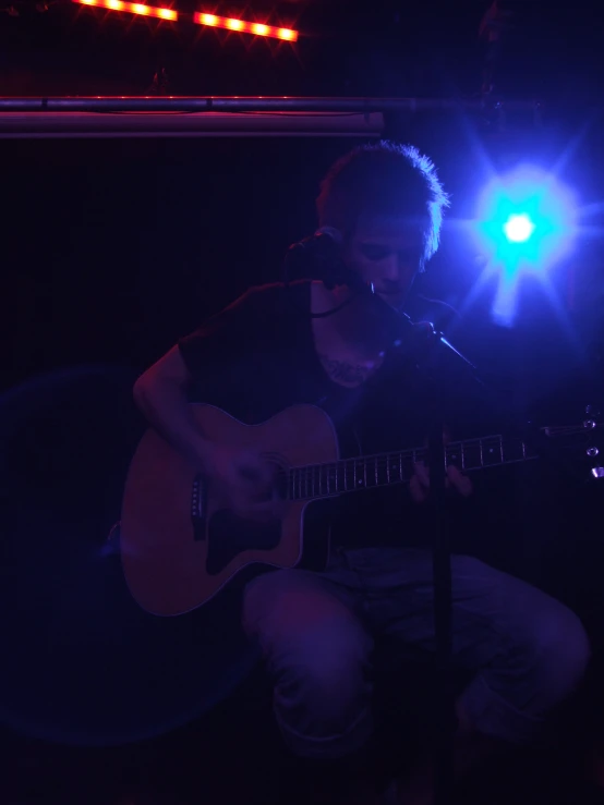 a man sitting down playing a guitar with blue lights