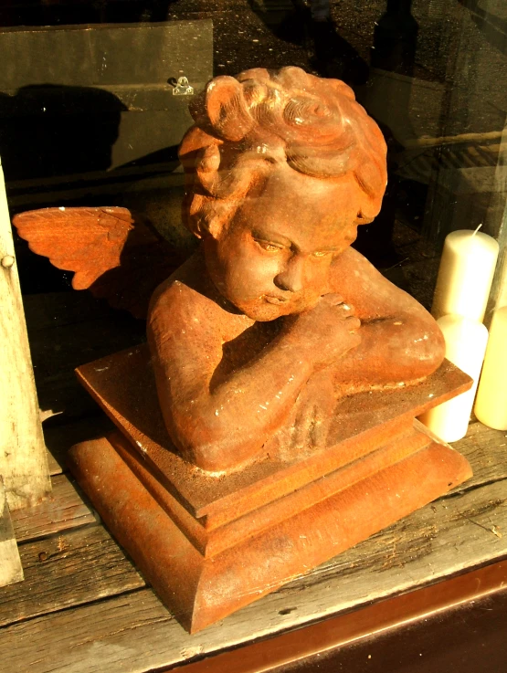 an orange clay angel statue with wings sitting inside a window