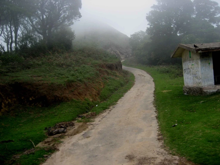 an empty dirt road near a small shack on a foggy day