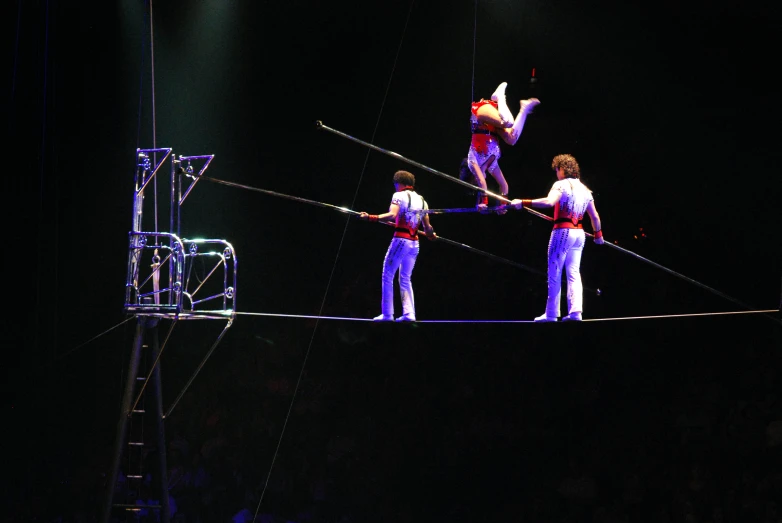 a group of people standing on a tight rope while holding onto sticks