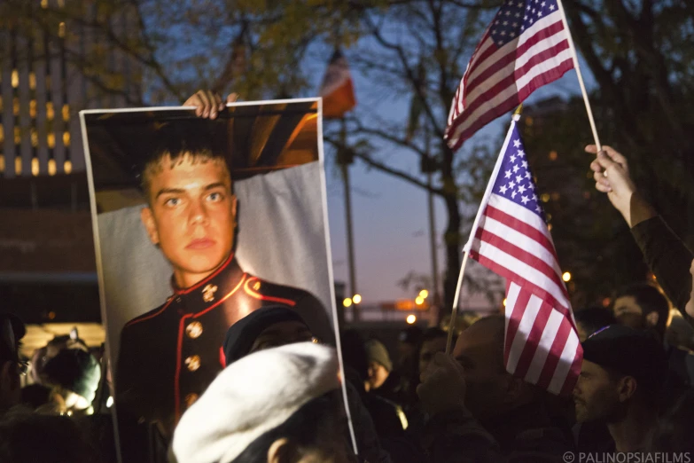 a crowd holding up american flags and portraits of military personnel