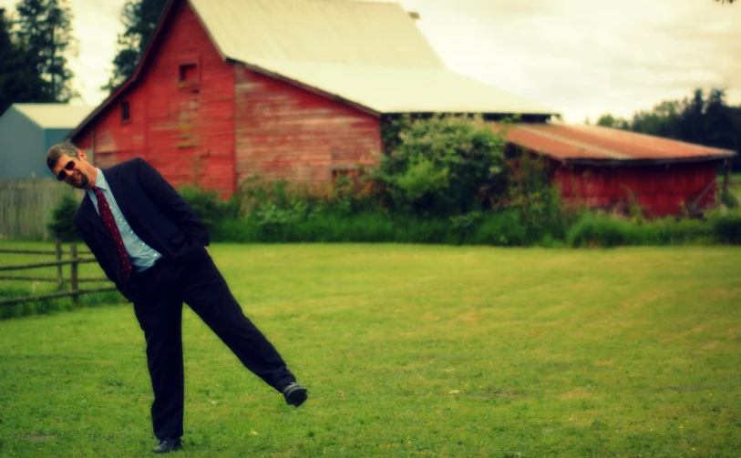 the man is wearing a suit and tie in front of a barn