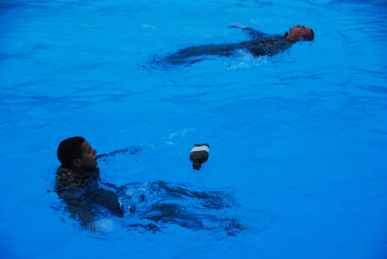 two people floating in a pool with water from a bottle