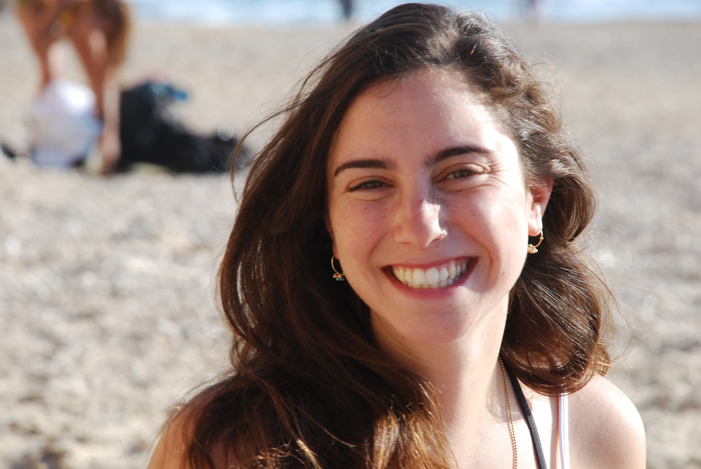 a girl sitting on the beach smiling at someone