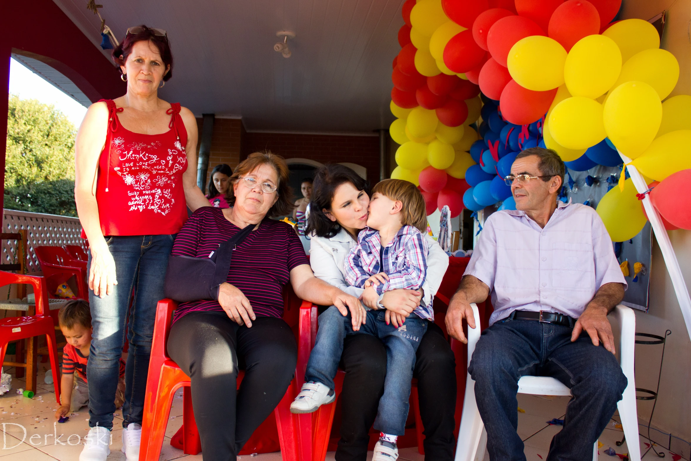the family poses in their red chair with their balloons hanging overhead